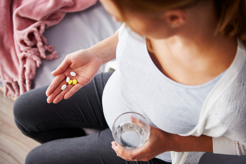 Menstrualna krema Menstra, škatlica protibolečinskih tablet, ženska masira trebuh, toplotna blazinica in krema